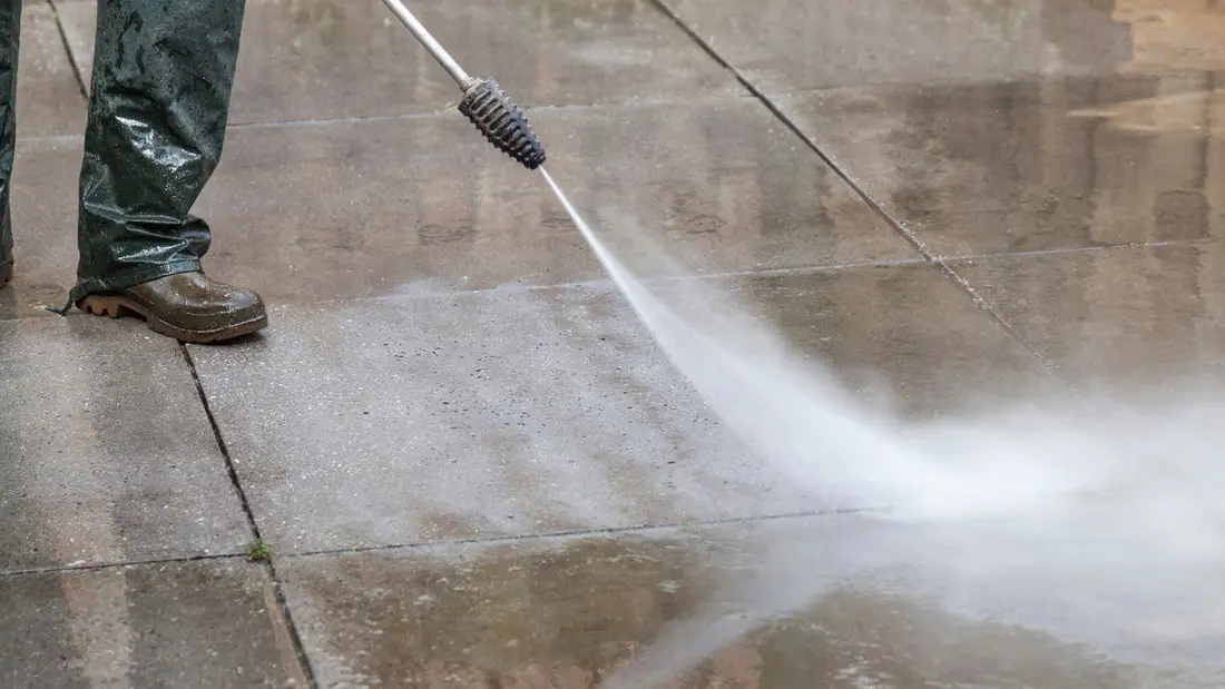 A pressure washer lifting moss and grime off a concrete surface