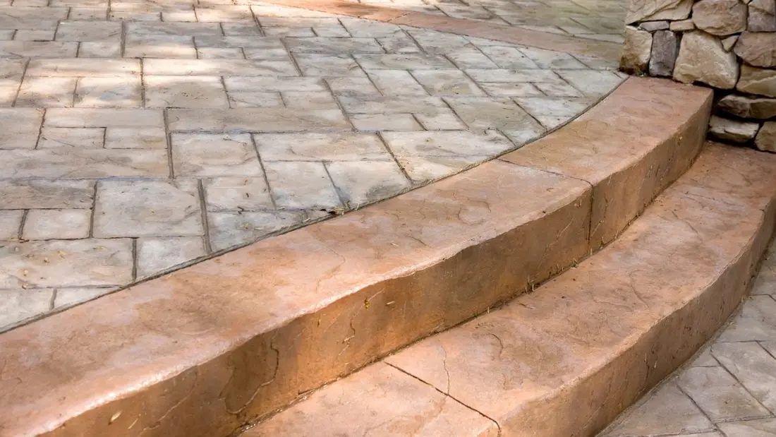 A stamped concrete patio with curved steps and a stone feature wall