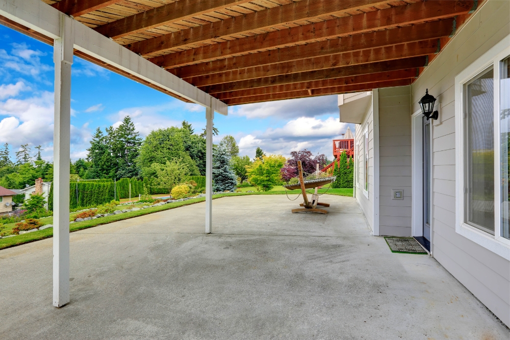 A large, open concrete patio area underneath a wooden second-storey deck